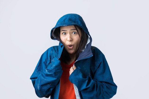 Retrato de una niña sonriente vestida con impermeable azul en gotas posando con capucha en gris