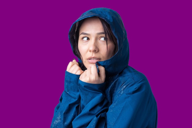 Retrato de una niña sonriente vestida con impermeable azul en gotas posando con capucha sobre fondo gris en un estudio