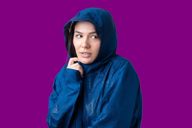 Retrato de una niña sonriente vestida con impermeable azul en gotas posando con capucha sobre fondo gris en un estudio