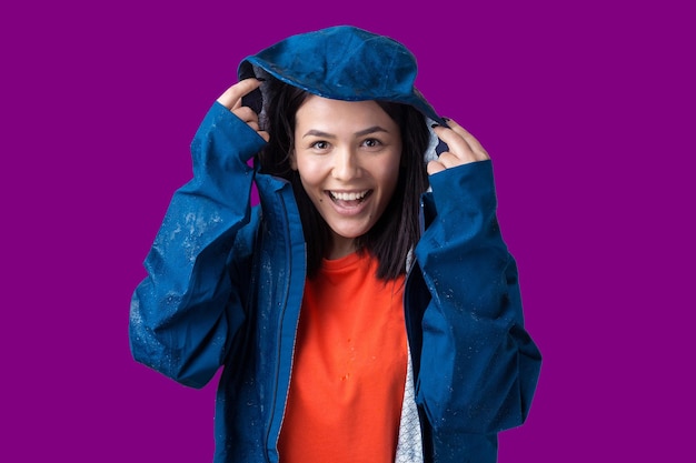 Retrato de una niña sonriente vestida con impermeable azul en gotas posando con capucha sobre fondo gris en un estudio