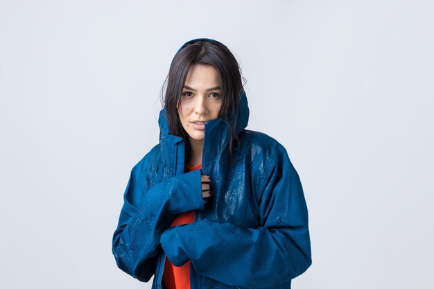 Retrato de una niña sonriente vestida con impermeable azul en gotas posando con capucha sobre fondo gris en un estudio.