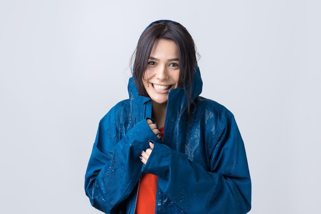 Retrato de una niña sonriente vestida con impermeable azul en gotas posando con capucha sobre fondo gris