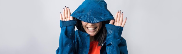 Retrato de una niña sonriente vestida con impermeable azul en gotas posando con capucha sobre fondo gris