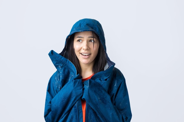 Foto retrato de una niña sonriente vestida con impermeable azul en gotas posando con capucha sobre fondo gris