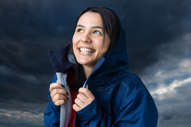 Retrato de una niña sonriente vestida con impermeable azul en gotas posando con capucha