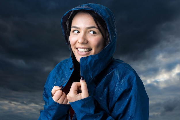 Retrato de una niña sonriente vestida con impermeable azul en gotas posando con capucha