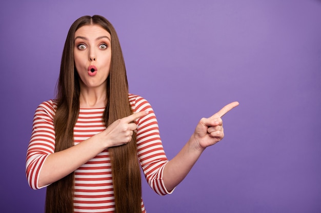 Retrato de niña sorprendida asombrada apunta el dedo índice copia espacio presente anuncios increíbles grito promocional wow Dios mío usa jersey de buena apariencia aislado sobre pared de color púrpura