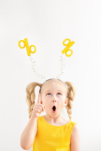 Retrato de niña sorprendida en una diadema con porcentajes amarillos en ella apareciendo con su dedo