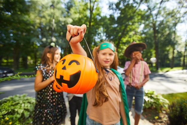 Retrato de niña sosteniendo la bolsa en forma de calabaza con dulces mientras está de pie al aire libre con sus amigos