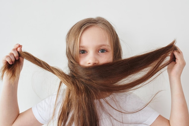 Retrato de niña sosteniendo el cabello en las manos sobre fondo blanco.