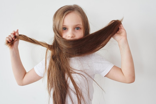 Retrato de niña sosteniendo el cabello en las manos sobre fondo blanco.