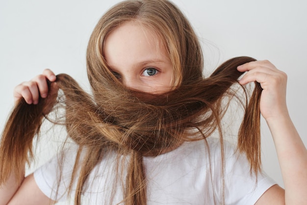 Retrato de niña sosteniendo el cabello en las manos sobre fondo blanco.