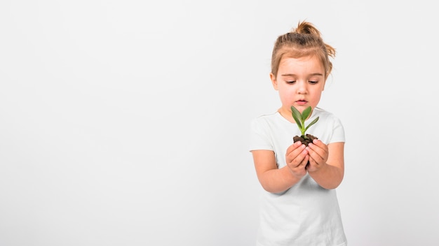 Foto retrato de una niña sosteniendo la planta de semillero en la mano contra el fondo blanco