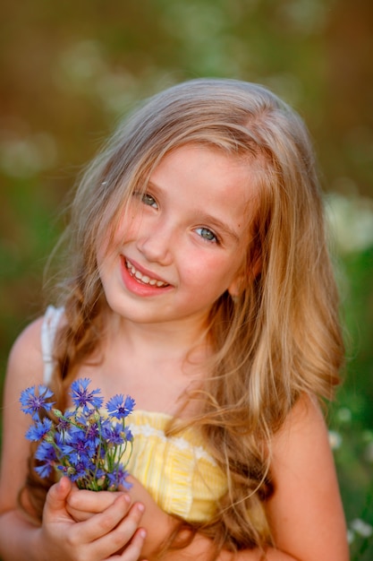 Retrato de una niña sosteniendo un ramo de flores azules en un campo en verano