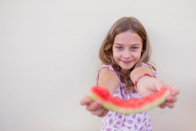 Foto retrato de una niña sosteniendo una sandía contra la pared