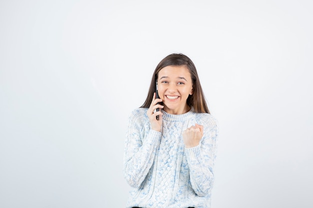 Retrato de niña en suéter de lana hablando con alguien por teléfono celular.