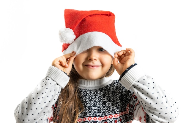 Retrato de niña en suéter de navidad de punto blanco con renos escondiendo media cara en santa claus ...