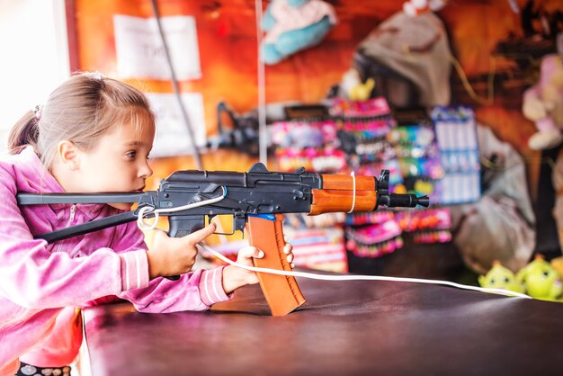 Retrato de niña en suéter rosa dispara desde pistola de juguete para niños.