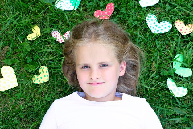 Un retrato de una niña tendida en el césped rodeada de corazones multicolores