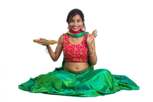 Foto retrato de una niña tradicional india sosteniendo diya, niña celebrando diwali o deepavali con la celebración de la lámpara de aceite durante el festival de la luz sobre la superficie blanca