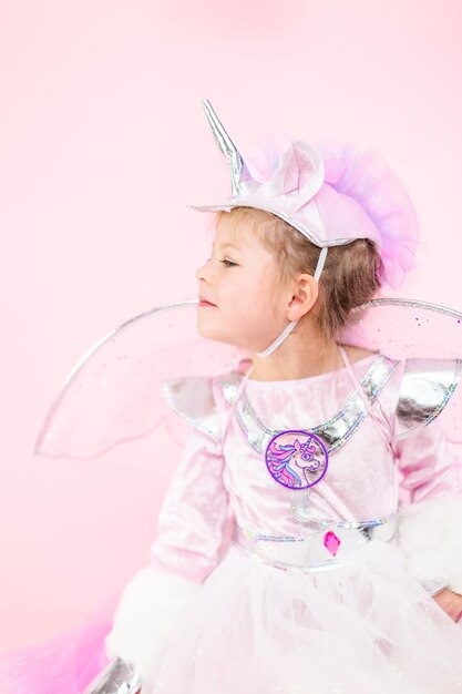 Retrato de una niña con traje de unicornio brillante sobre fondo rosa.