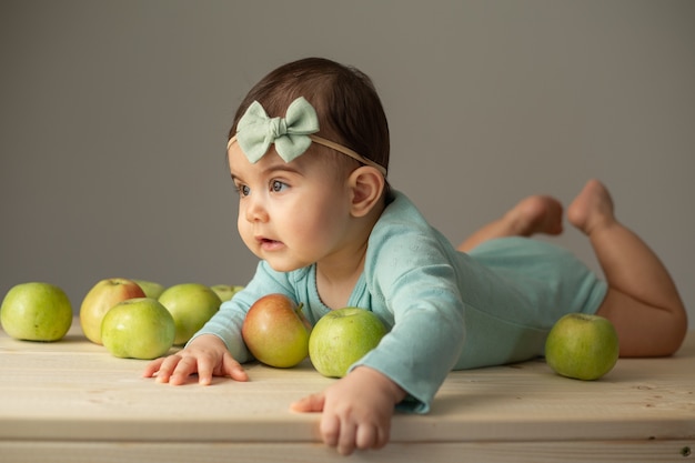 Retrato de una niña en un traje verde sobre una mesa de madera con manzanas verdes frescas. Productos naturales para niños. Foto de alta calidad