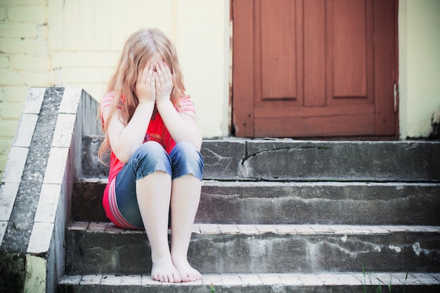 Retrato de niña triste sentada cerca de la pared