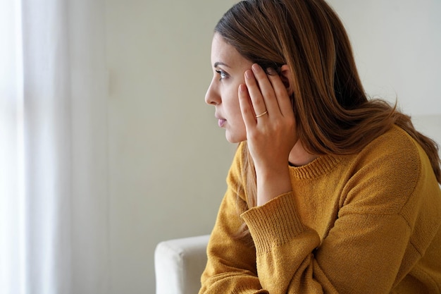 Retrato de niña triste y solitaria en casa mirando a través de la ventana Salud mental ansiedad pensamiento deprimido adolescente