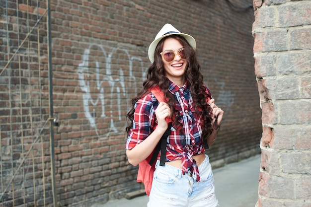 Retrato de una niña turista con sombrero y gafas de sol en el callejón trasero de ladrillo rojo.