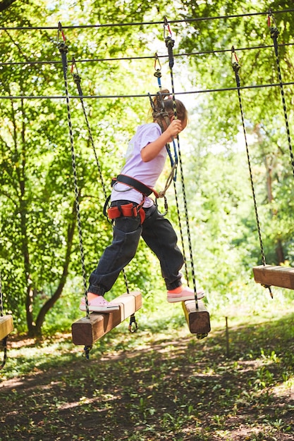 Foto retrato de una niña valiente caminando sobre un puente de cuerda en un parque de cuerdas de aventuras divirtiéndose en el parque de aventuras scout practicando rappel