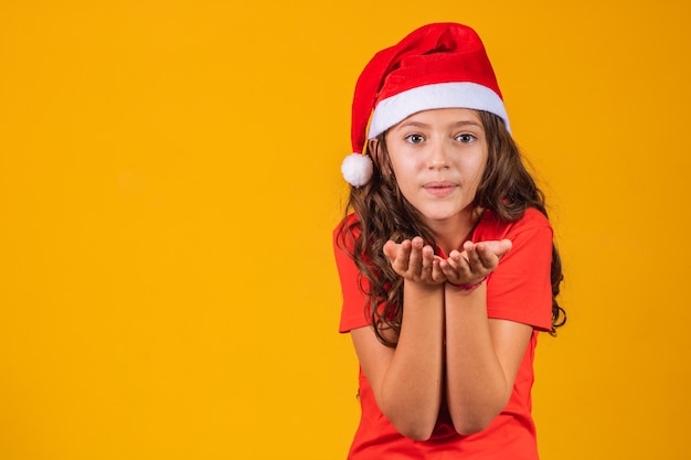 Retrato de una niña vestida con ropa de Navidad que sopla algo en sus manos.