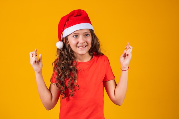 Retrato de una niña vestida con traje de Navidad con los dedos cruzados deseando suerte.