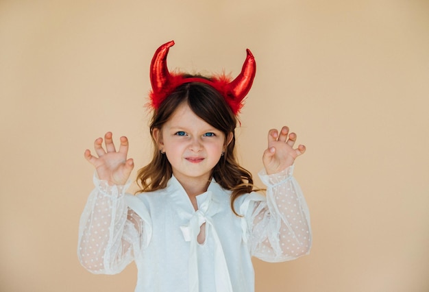 Retrato de una niña con un vestido blanco con cuernos de diablo Disfraz de Halloween Estado de ánimo enojado Una expresión amenazante en su rostro