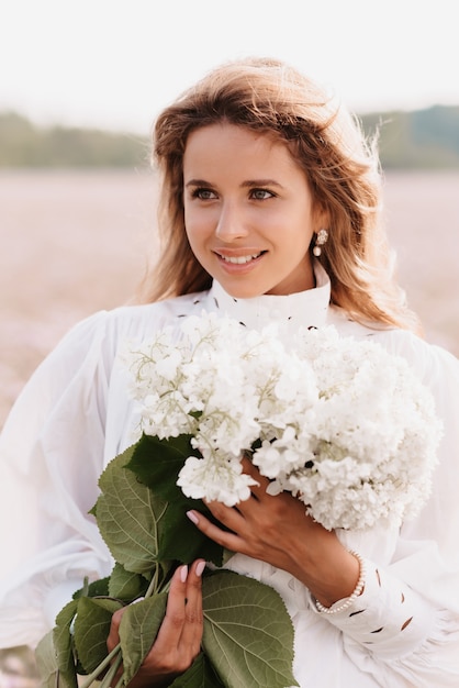 Retrato de una niña con un vestido blanco con un ramo de flores en verano en la naturaleza en el campo