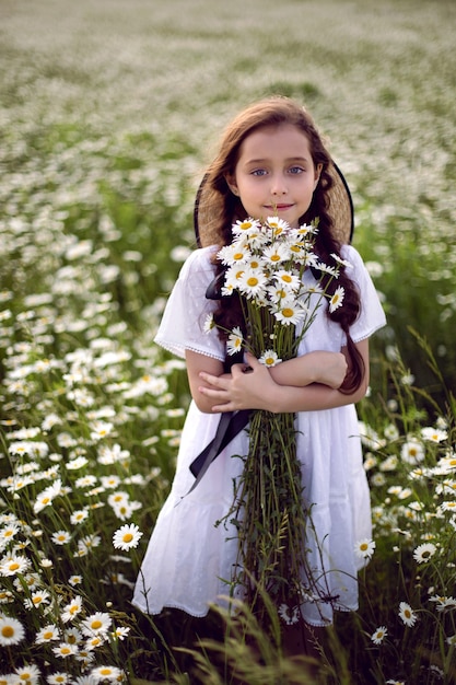 Retrato de niña con un vestido blanco con sombrero en el campo de flores
