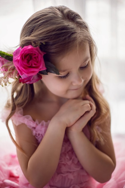 El retrato de una niña con un vestido rosa y una flor con una rosa en la cabeza y una red se filma en el estudio