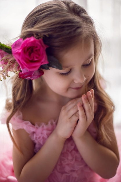 El retrato de una niña con un vestido rosa y una flor con una rosa en la cabeza y una red se filma en el estudio