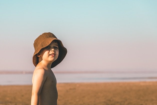 Retrato de un niño de 3 años con un sombrero de Panamá marrón en la playa. Copia espacio