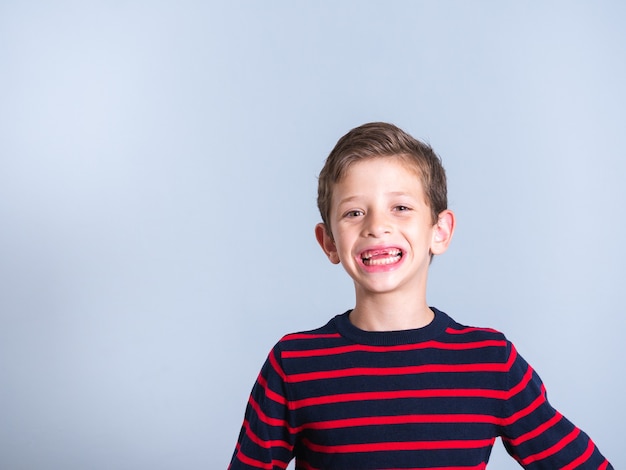 Retrato de un niño de 7 años a quien le falta un diente frontal, aislado sobre un fondo gris, con espacio de copia