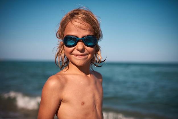 Retrato de un niño de 8 años de pelo largo con gafas de natación contra el fondo del mar en una noche de verano