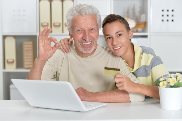 Retrato de niño y abuelo con una computadora portátil y una tarjeta de crédito en casa