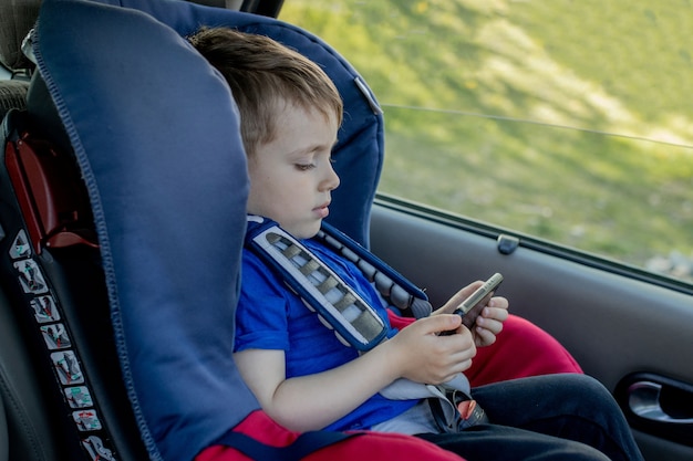 Retrato de un niño aburrido sentado en un asiento de seguridad. Seguridad del transporte de niños