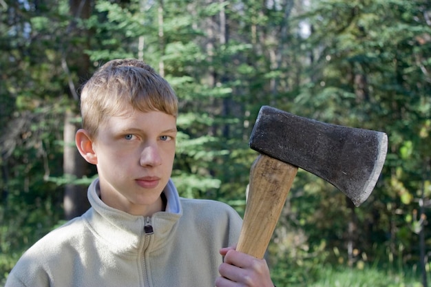 Retrato de un niño adolescente sosteniendo un hacha contra los árboles en el bosque