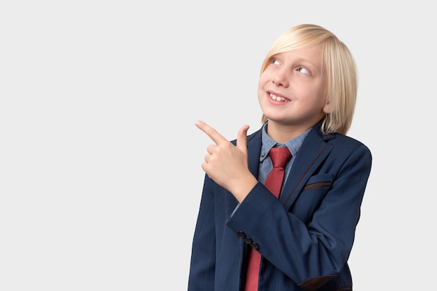 Retrato de un niño adolescente en uniforme escolar apuntando al espacio de copia y mirando a un lado aislado sobre un fondo blanco