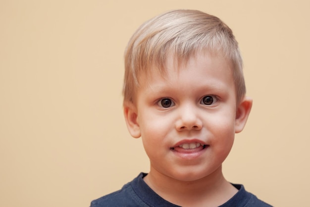 Retrato de niño adorable con ojos marrones posando para la cámara sobre fondo beige en estudio