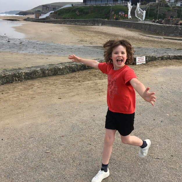 Foto retrato de un niño alegre con los brazos extendidos corriendo por la playa