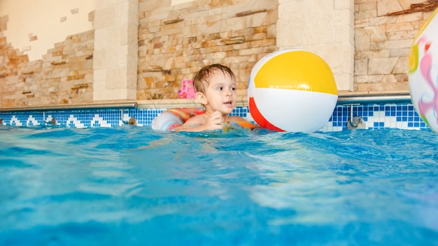 Retrato de niño alegre feliz jugando con una pelota de playa inflable y un colorido anillo en la piscina cubierta de la casa