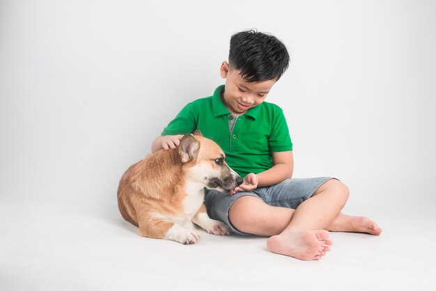 Retrato de un niño alegre que se divierte con el perro Welsh Corgi en el suelo