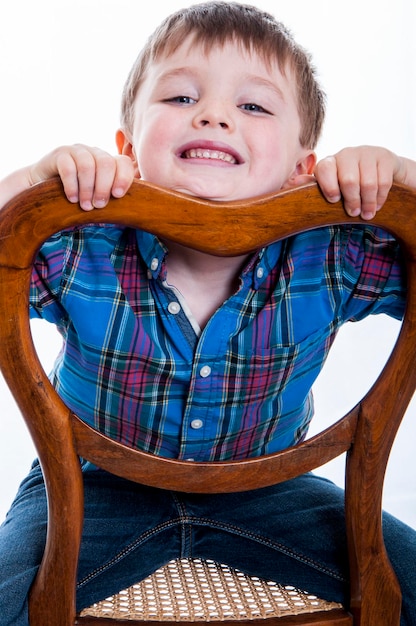 Retrato de un niño alegre sentado en una silla de madera contra un fondo blanco