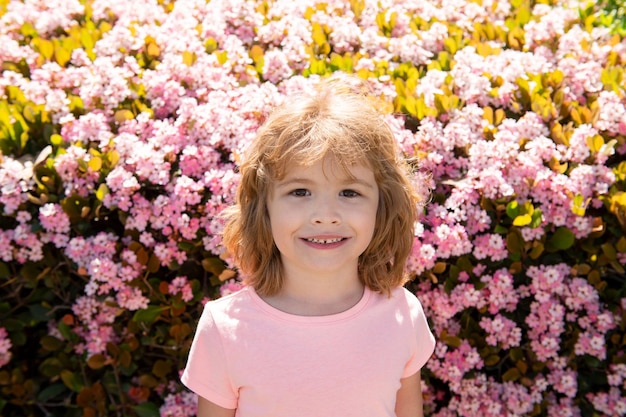 Retrato de niño alegre sobre fondo de parque de primavera flor. Niño chico lindo alegre.